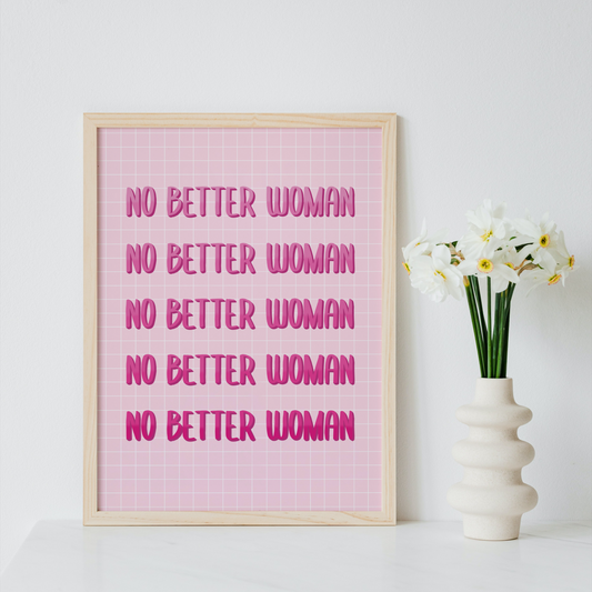 A framed typographic wall art print with the phrase 'NO BETTER WOMAN' repeated in pink text on a pink grid background, leaning against a white wall beside a white vase with white flowers.