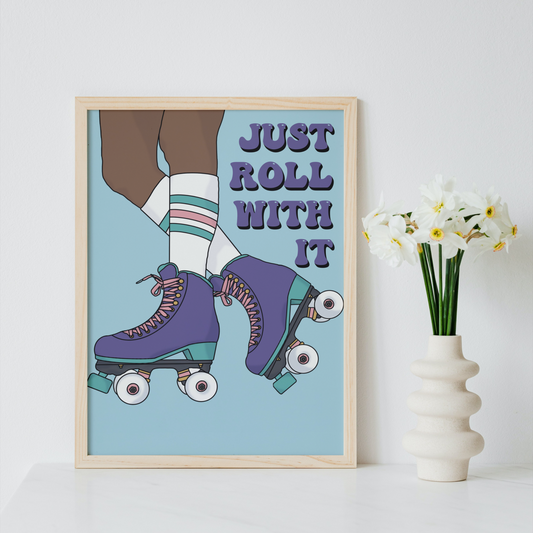 A framed art print featuring a retro illustration of roller skates and the text 'JUST ROLL WITH IT' leans against a white wall next to a white vase with white flowers.