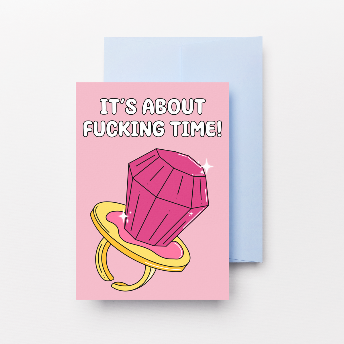 A pink greeting card with a cartoon pink ring pop on a yellow ring and the text 'IT'S ABOUT FUCKING TIME!' stacked on top of a light blue envelope against a light gray background.