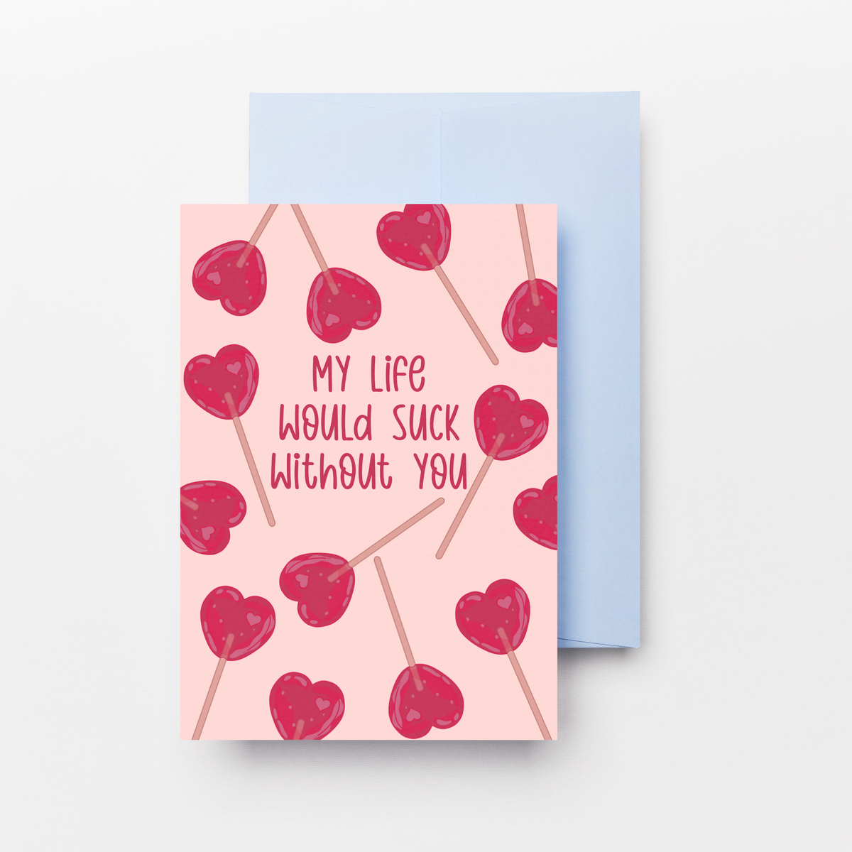A greeting card with a pink background, red heart illustrations, and the text 'MY LIFE WOULD SUCK WITHOUT YOU', shown with a light blue envelope behind it on a white background.
