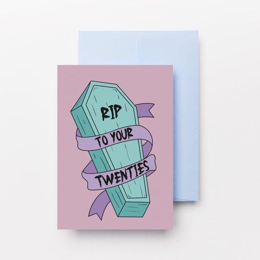 A square greeting card with a lavender front featuring a cartoon coffin and the text 'RIP TO YOUR TWENTIES' in black, shown with a light blue envelope behind it on a white background.