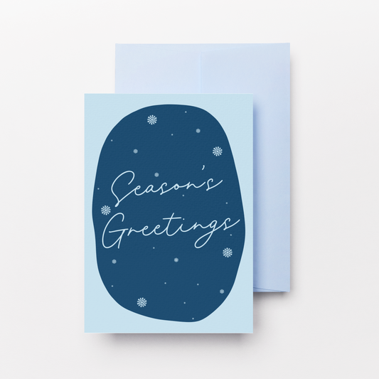 A light blue greeting card with a dark blue oval graphic and the words 'Season's Greetings' in white script, shown with a matching light blue envelope on a clean white background.