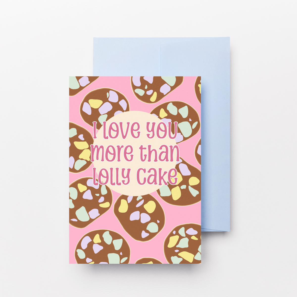 A pink greeting card with a lolly cake pattern and the text 'I love you more than lolly cake' in pink script, shown with a light blue envelope on a white background.