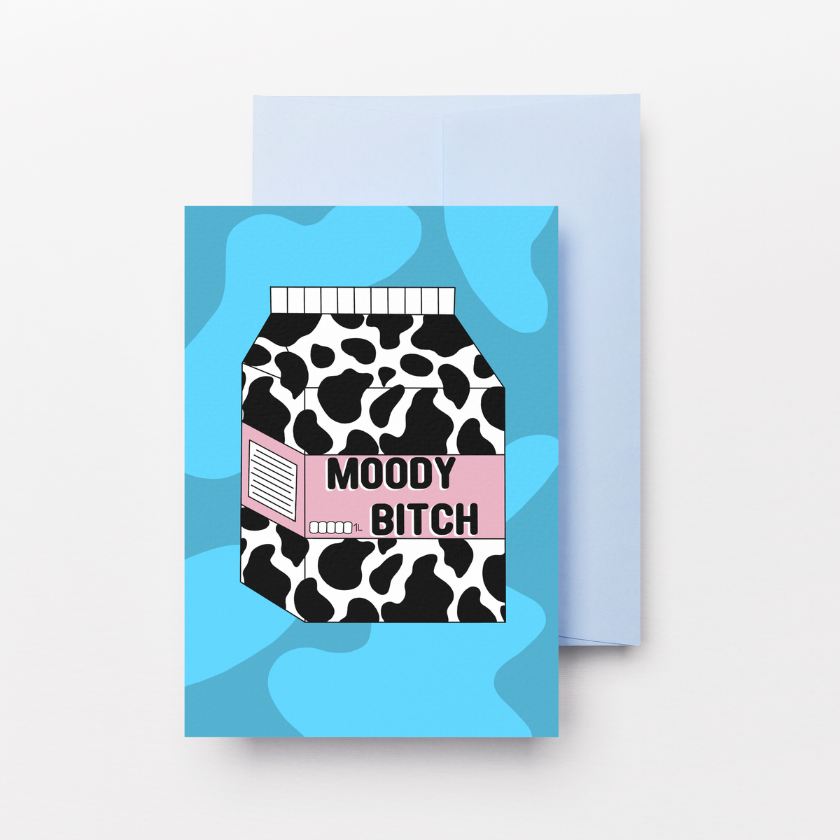 A greeting card with a light blue envelope behind it, featuring a graphic of a milk carton with a black and white cow print, a pink stripe, and the text 'MOODY BITCH' on a light blue abstract background.