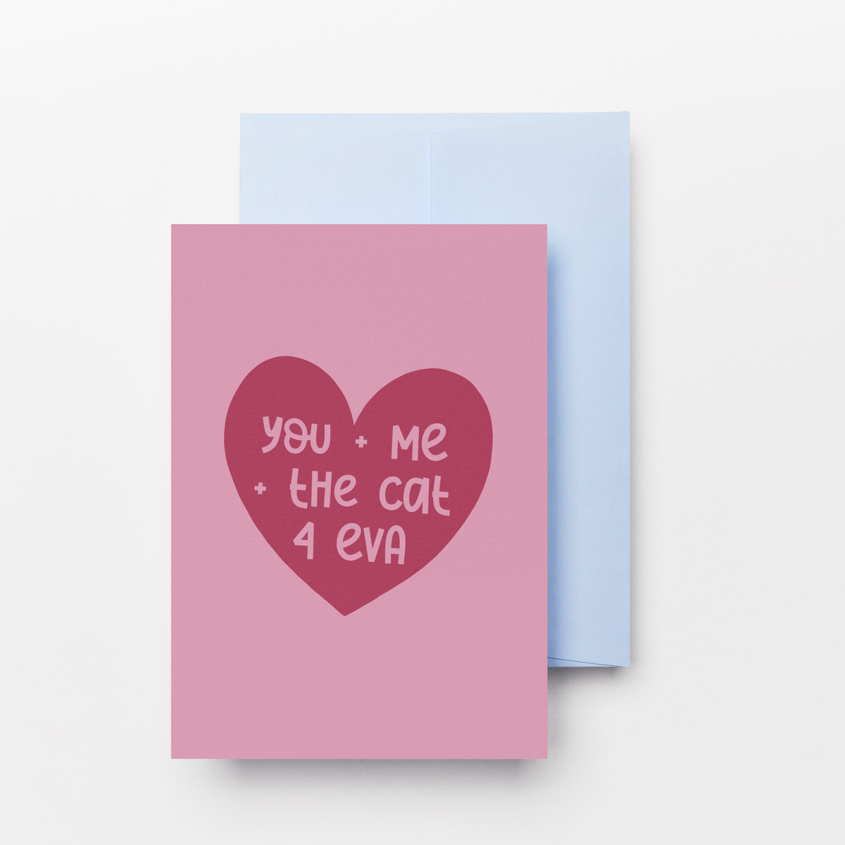 A pink greeting card with a dark red heart graphic containing the text 'you - Me - the cat 4 eva' in pink, shown with a light blue envelope behind it on a clean white background.