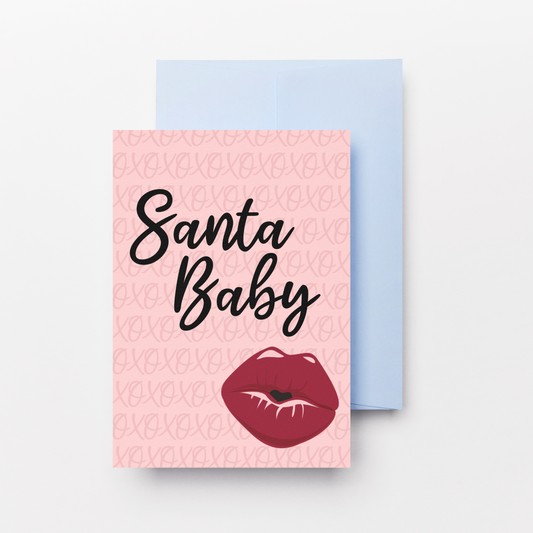 A pink greeting card with a light blue envelope behind it, featuring the words 'Santa Baby' in black script and a red lips graphic at the bottom.