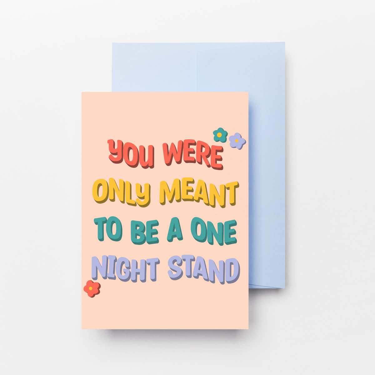A peach-colored greeting card with colorful playful text reading 'YOU WERE ONLY MEANT TO BE A ONE NIGHT STAND' in red, yellow, teal, and purple lettering, shown with a light blue envelope behind it on a light gray background.